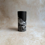 A black cylindrical container with a lid, featuring a printed graphic of a snowy mountain landscape with gold glitter accents, set against a textured beige background.